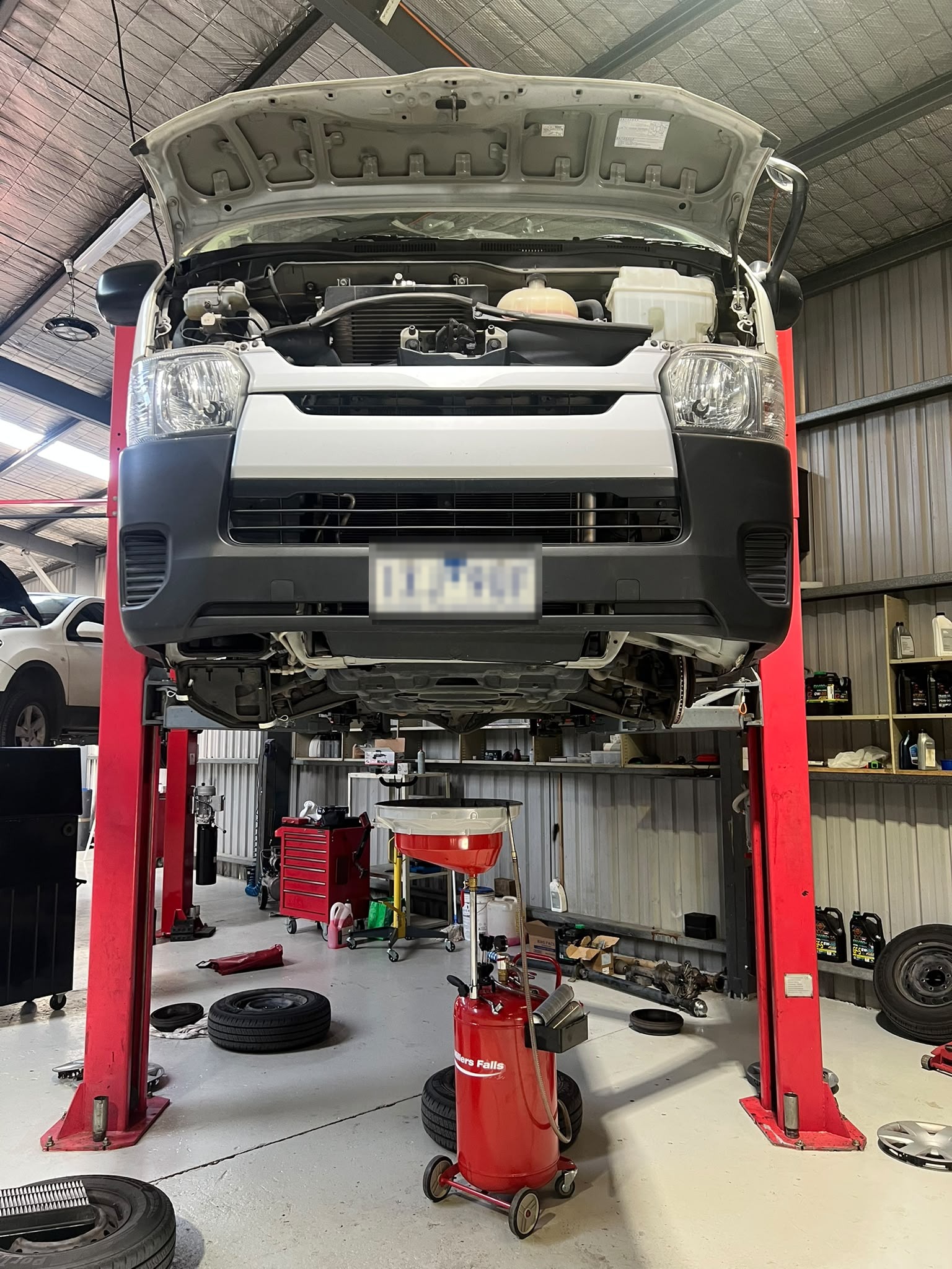 Technician servicing a vehicle engine bay on a hoist